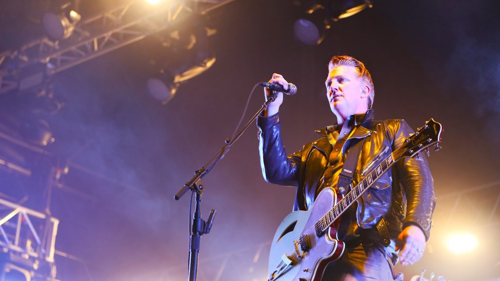 Josh Homme singing and playing electric guitar on stage
